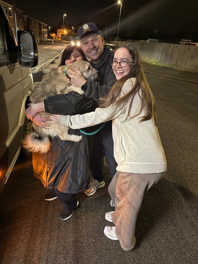 A family greeting their rescue dog by the van on arrival night, with the driver looking on.