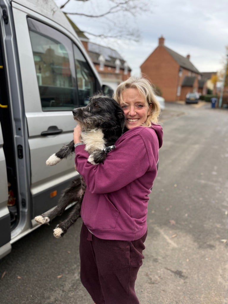 A smiling adopter hugging her rescue dog at the van door, moments after delivery.
